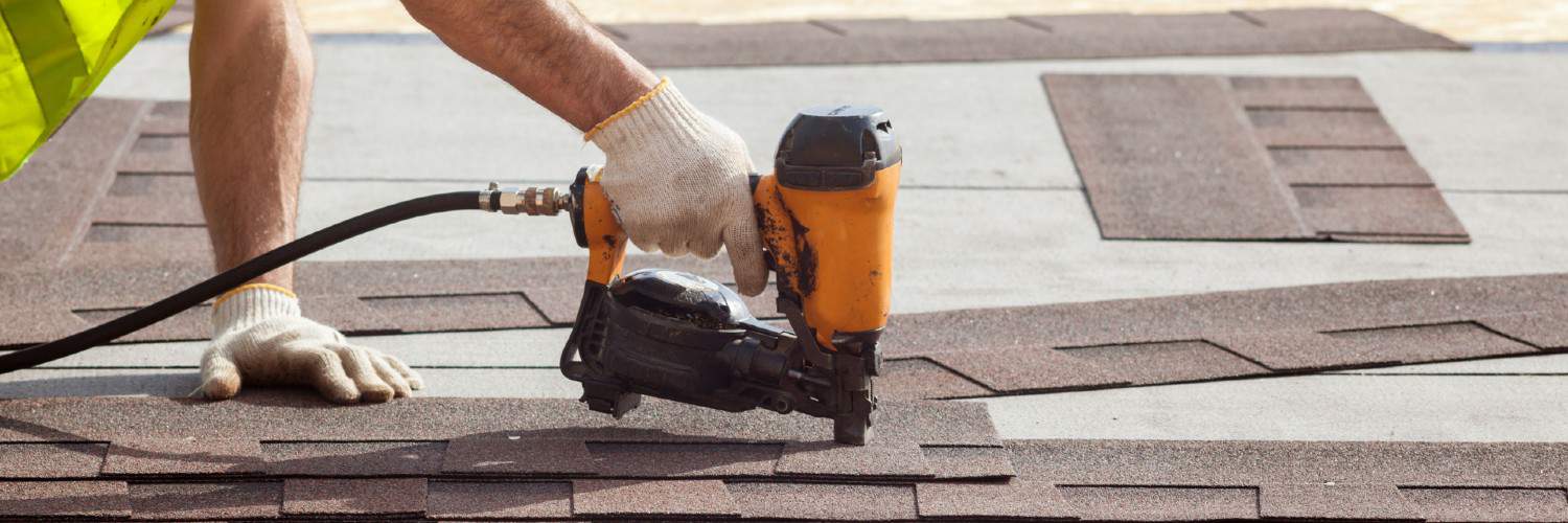 a worker using a nail gun to nail shingles to a roof