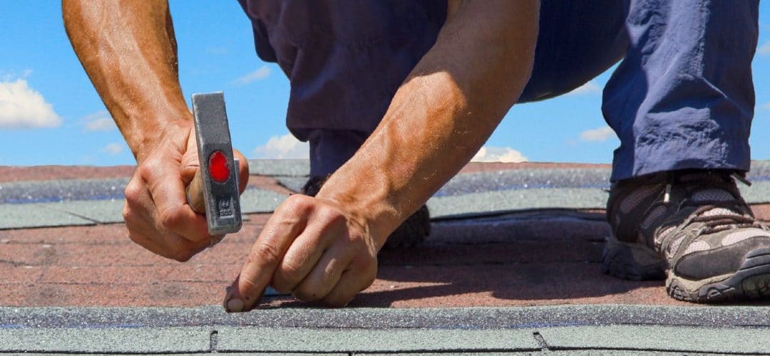 a worker hammering nails into a shingle on a roof