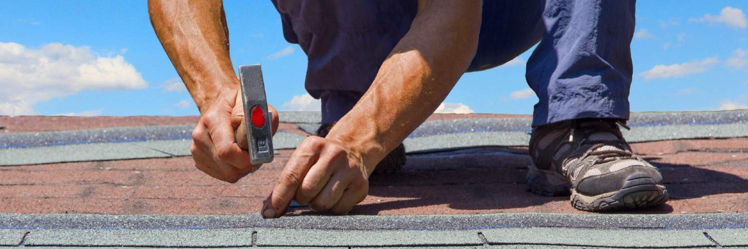 a worker hammering nails into a shingle on a roof